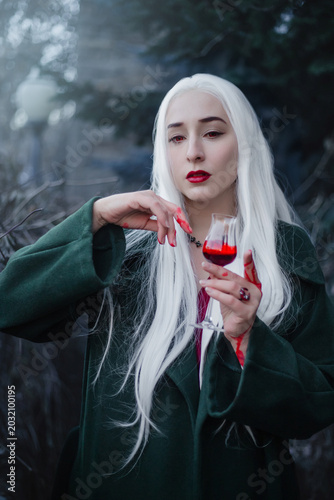 A gothic vampire with bloody hands and a mystical look drinks from a glass.