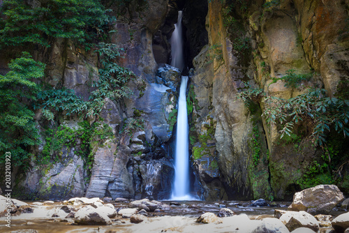 Salto do Cabrito waterfall flowing through a narrow rocky canyon surrounded by green vegetation on Sao Miguel Island, Azores, Portugal.