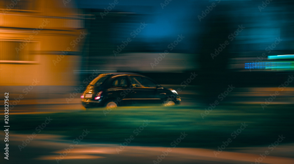 Obraz premium Dark small car travels quickly on an urban street at night Buildings blurred by fast movement