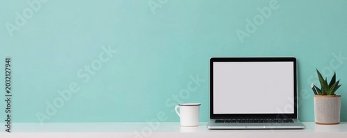 Clean and minimalist desk setup Laptop mockup, white mug and desk plant on a white table with a vibrant turquoise wall. Modern home office workspace, ample copy space. productivity,