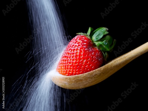  Sugar pouring on a strawberry on wooden spoon.