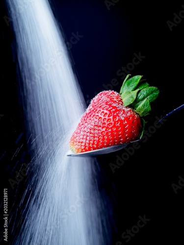  Sugar pouring onto a ripe strawberry.