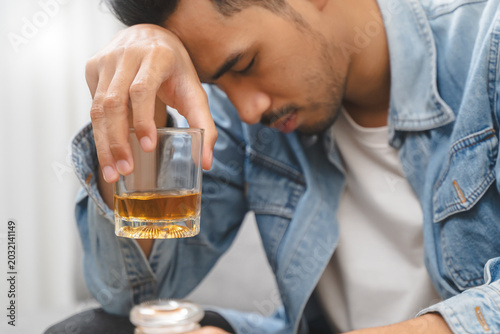 Tableau sur toile melancholy young Asian man drinks alcoholic whisky alone at home feeling dizzy a