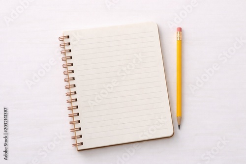 Top view of a blank lined spiral notebook with a yellow pencil on white background