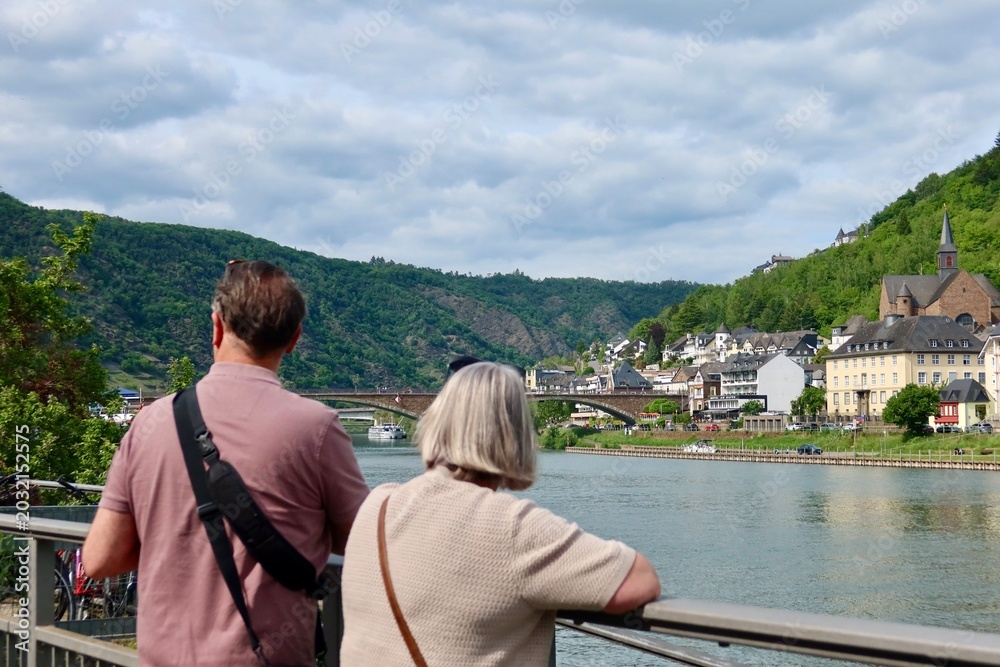 Fototapeta premium Tourists enjoying the scenic Moselle River view in Cochem, Germany. Green hills and riverside houses create a peaceful atmosphere.