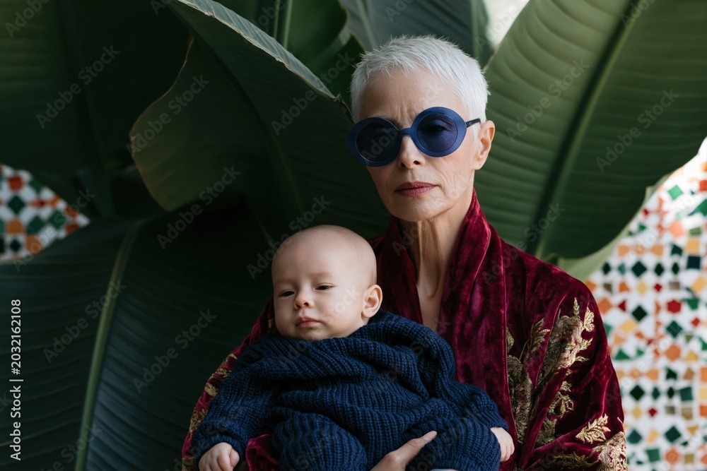 Naklejka premium Elderly woman holding baby in botanical courtyard setting