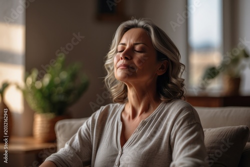 Middle aged woman meditating at home with eyes closed, relaxing body and mind in a living room
