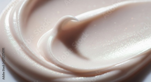 A detailed macro close-up of a smooth, thick cosmetic cream or lotion texture with a soft pinkish or beige tint, showing a perfect swirl