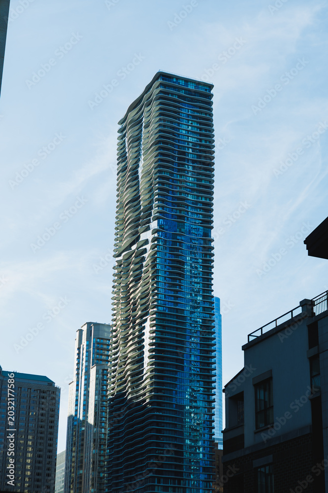Fototapeta premium Tall building with a unique design stands against a bright sky in an urban area during the daytime