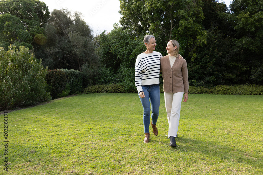 Fototapeta premium Senior and middle-aged women walking on manicured lawn in private garden wearing ankle boots