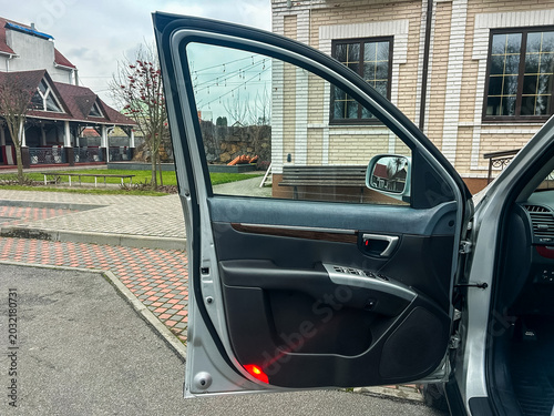 Canvas Print Door of a silver car open in a driveway near a house with a garden and playgroun