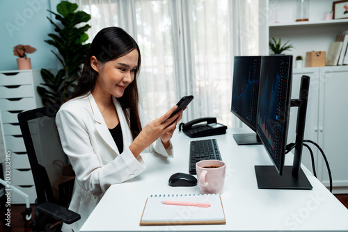 Quadro em tela Smiling young Asian businesswoman with happy face looking on smartphone in profitable of exchange stock market graph at modern office