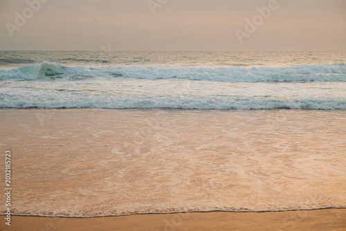 Quadro su tela Waves wash ashore on sandy beach during evening light near ocean