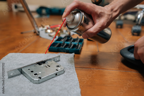 Tableau sur toile Male hand lubricating door lock mechanism with spray oil, performing home maintenance or diy repair work to prevent sticking and extend hardware lifespan in domestic setting
