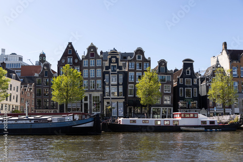 Billede på lærred Ortsbild in Amsterdam, Häuser am Wasser mit Hausbooten davor