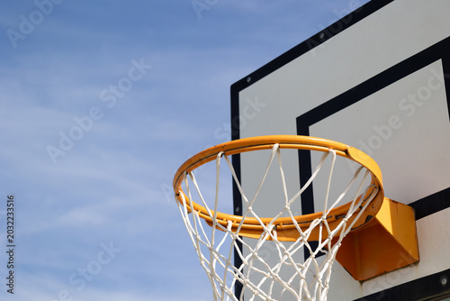 Outdoor basketball hoop with white net and orange rim against a clear blue sky.

