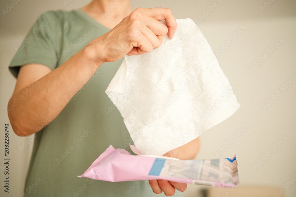 Fototapeta premium Woman hands holds white wet tissue above pink packaging. Home cleaning routine, lifestyle concept