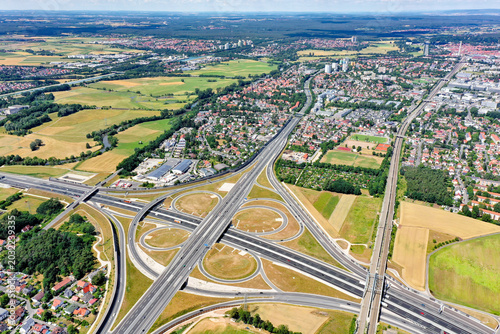 Aerial view of the A73 highway interchange with cloverleaf ramps, surrounding green fields, and residential neighborhoods in Nurnberg, Bayern, Germany.