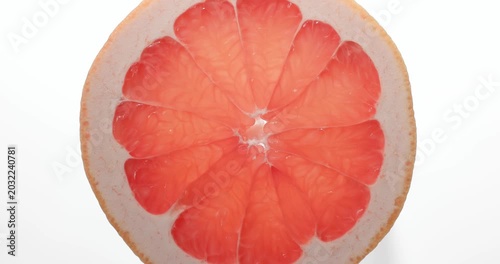 Macro top view close-up shot of a fresh round red grapefruit slice rotating slowly. The vibrant citrus fruit slice spins smoothly, showcasing its juicy pulp, detailed texture, and natural patterns