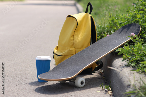 Photos Skateboard, yellow backpack and coffee on the side of the road