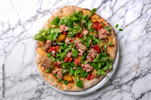 Slika na platnu Fusion gourmet pizza with tuna, lamb’s lettuce, cherry tomatoes and olives served on artisan crust isolated on marble background