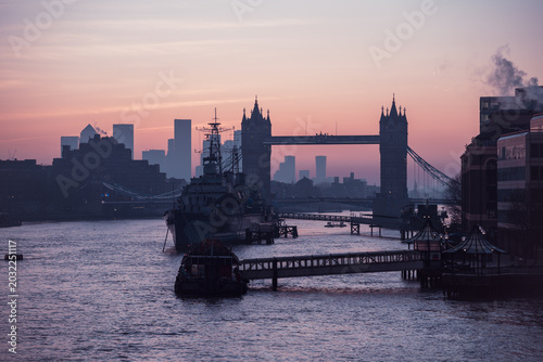 Fotografie The sun rises over the River Thames, casting silhouettes of HMS Belfast and Tower Bridge