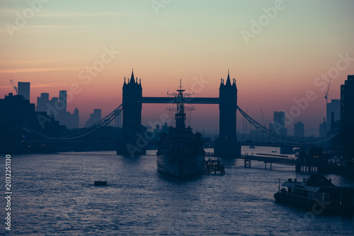 Quadro su tela The sun rises over the River Thames, casting silhouettes of HMS Belfast and Tower Bridge