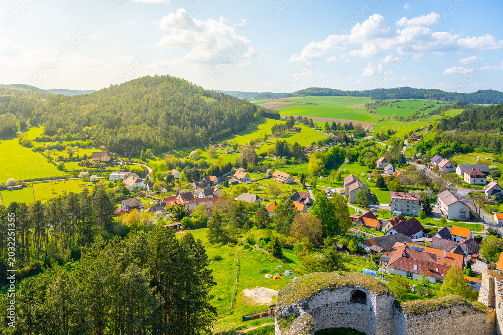 Fototapeta premium The lookout from Rabi Castle shows the green hills and small houses below. Surrounding fields stretch far into the distance under a clear blue sky. Nature and village are visible together.