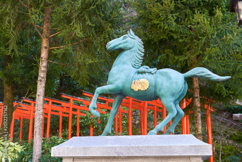 Quadro su tela A verdigris bronze statue of a prancing horse stands on a gray stone pedestal in a Japanese shrine setting
