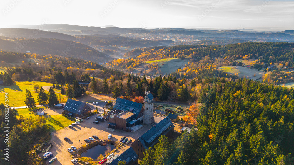 Fototapeta premium Kralovka Lookout Tower stands tall amidst vibrant autumn colors in the Jizera Mountains. Visitors enjoy stunning views in the serene landscape as the season changes.