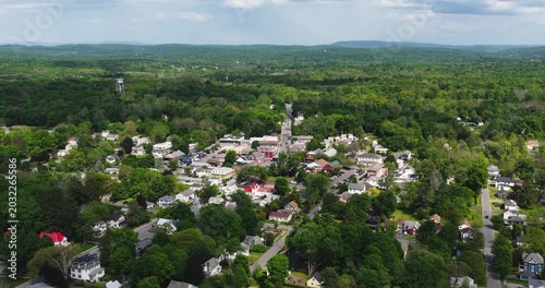 Red Hook, NY, USA - 05-20-2026  Aerial video of a small town nestled within a vast expanse of lush green forest under a partly cloudy sky.