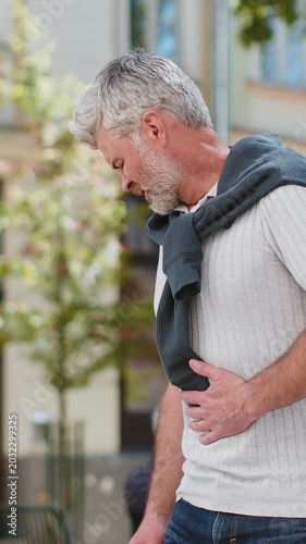 Caucasian mature man feeling sudden strong abdominal stomach ache, gastritis problem. Upset tourist guy having symptom poisoning diarrhea indigestion peptic ulcer pancreatitis on city urban street.