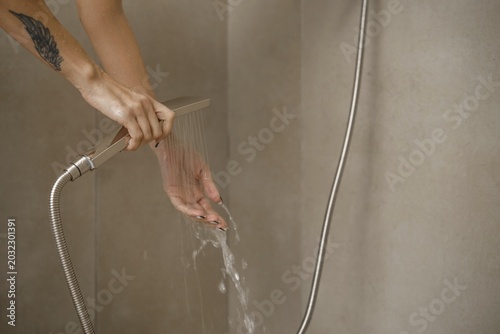 Hands are positioned under flowing water from a sleek showerhead in a stylish bathroom. The setting features clean lines and neutral walls, emphasizing a relaxing ambiance during personal care