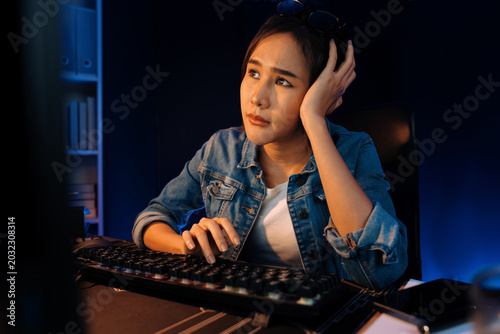 Tableau sur toile Stressful young beautiful asian creative looking on pc to search project creator social media online with planning channel strategy reach of more viewer home at neon modern office at night