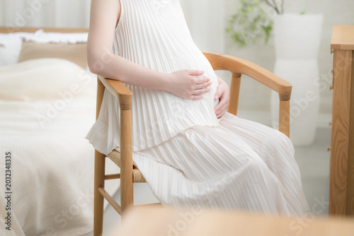Foto 笑顔でお腹に手を添える日本人女性の妊婦さん、マタニティライフスタイルイメージの笑顔で座る　顔無しの手元のクローズアップ