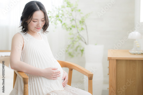 Fotografie 笑顔でお腹に手を添える日本人女性の妊婦さん、マタニティライフスタイルイメージのうつむく笑顔