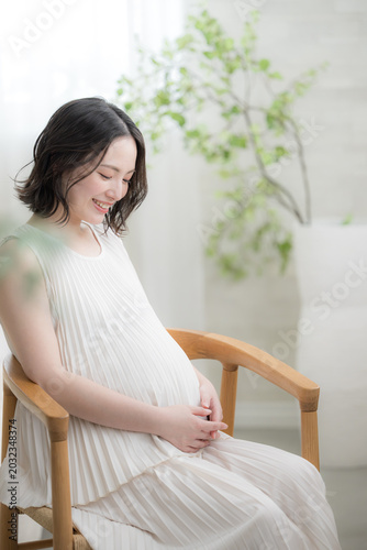 笑顔でお腹に手を添える日本人女性の妊婦さん、マタニティライフスタイルイメージの笑顔で座る