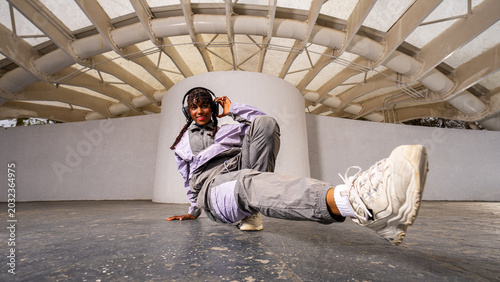 Quadro su tela Young afro latina woman performing street dance pose with headphones in urban se