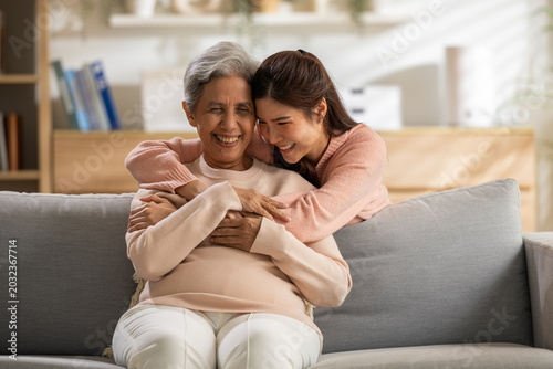 Happy family mother and adult daughter hug with deep love and joyful emotion on sofa in comfortable living room, senior woman smiling feeling strong affectionate bonding together at cozy home