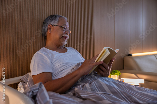 Tableau sur toile Senior man reading book bed bedroom eyeglass evening home relaxation Senior man