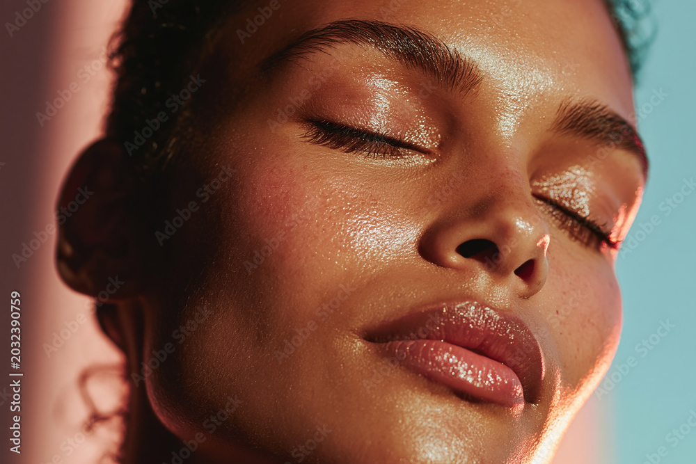 Fototapeta premium Glowing complexion close up portrait of woman with dewy skin, closed eyes, soft makeup, and relaxed expression in warm directional light
