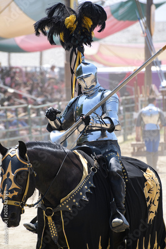 Fotografía A knight in polished silver armor rides a black horse during a medieval jousting