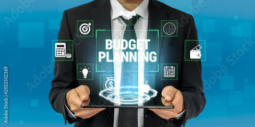 Fotografie Businessman in Suit Holding Tablet with Icons Representing Budget Planning, Finance, and Strategy in Modern Digital Environment Fluxor