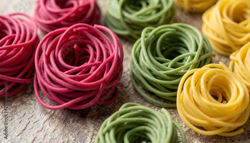 Fresh colorful pasta nests with flour and egg on rustic wooden table. Creative Italian food concept with spinach, beetroot, and classic pasta varieties.
