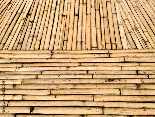 Obraz na płótnie The image shows a light brown bamboo bridge, beautifully constructed from split bamboo stalks assembled into a walkway amidst a variety of colorful and naturally arranged ornamental flowers