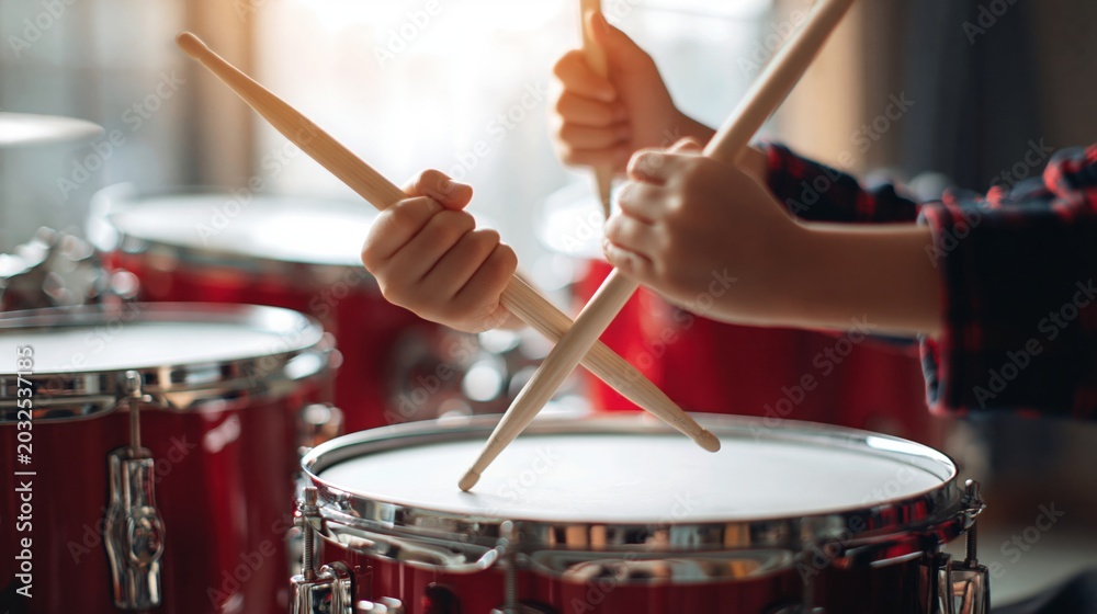 Obraz premium Close up of hands holding drumsticks playing a red drum set with bright studio lighting