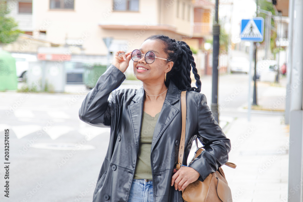 Fototapeta premium Fashionable young African woman with handbag in casual, stylish black girl posing in the city