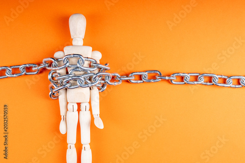 Foto Chained wooden figure on orange backdrop, oppression and loss of autonomy symbol