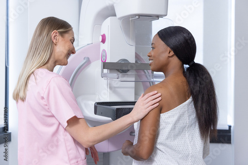 Fotografi Female tech in pink scrubs guiding African-American woman undergoing mammography