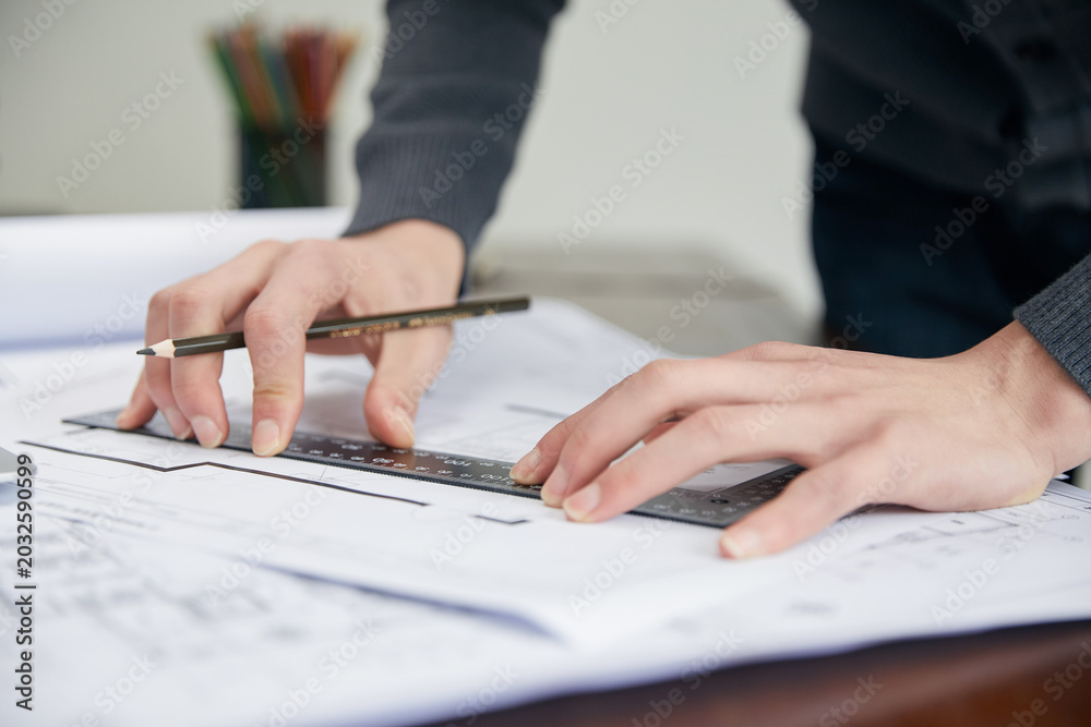 Fototapeta premium Architect Reviewing Construction Drawings with Ruler and Pencil